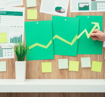 Businessman composing a successful financial chart with arrow going up, he is using green paper cuts, eco business and financial success concept